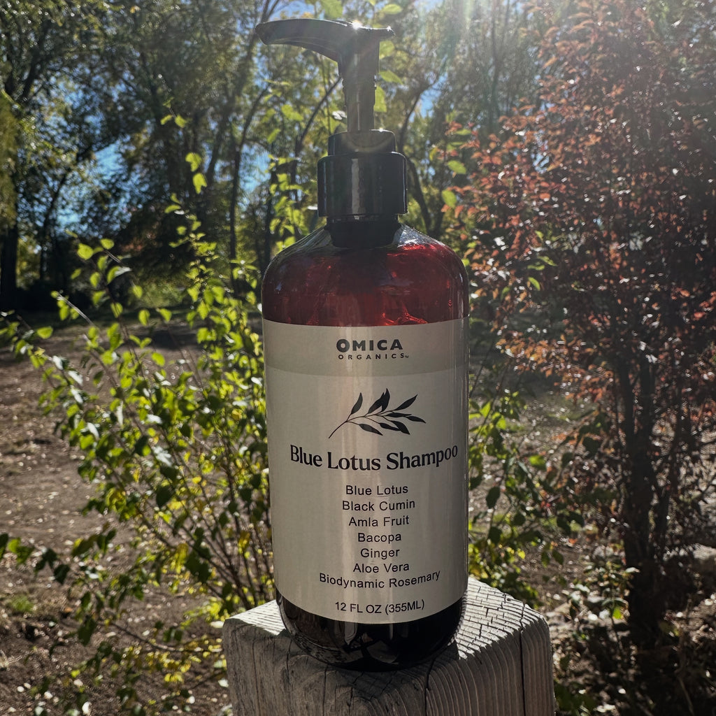 Bottle of Omica Organics Blue Lotus Shampoo on a wooden block with trees in the background